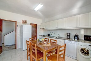 A compact kitchen with white cabinets, a built-in dishwasher, a washing machine, and a dining area with wooden chairs and a table.