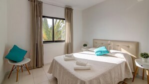 A bedroom with a bed, a chair, a nightstand, and a window with curtains. - Vila Casa do Cerro with Pool, Garden & Wi-Fi (Boliqueime)