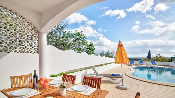 An outdoor dining area with a pool, wooden chairs, and a table set for two. - Vila Casa do Cerro with Pool, Garden & Wi-Fi (Boliqueime)