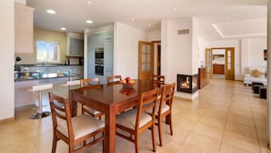 Uma sala de estar ampla com uma mesa de jantar, cadeiras, lareira e uma cozinha ao fundo.