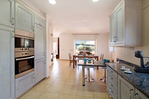 Una cocina con electrodomésticos integrados, un comedor con mesa y sillas, y vistas a través de una ventana.