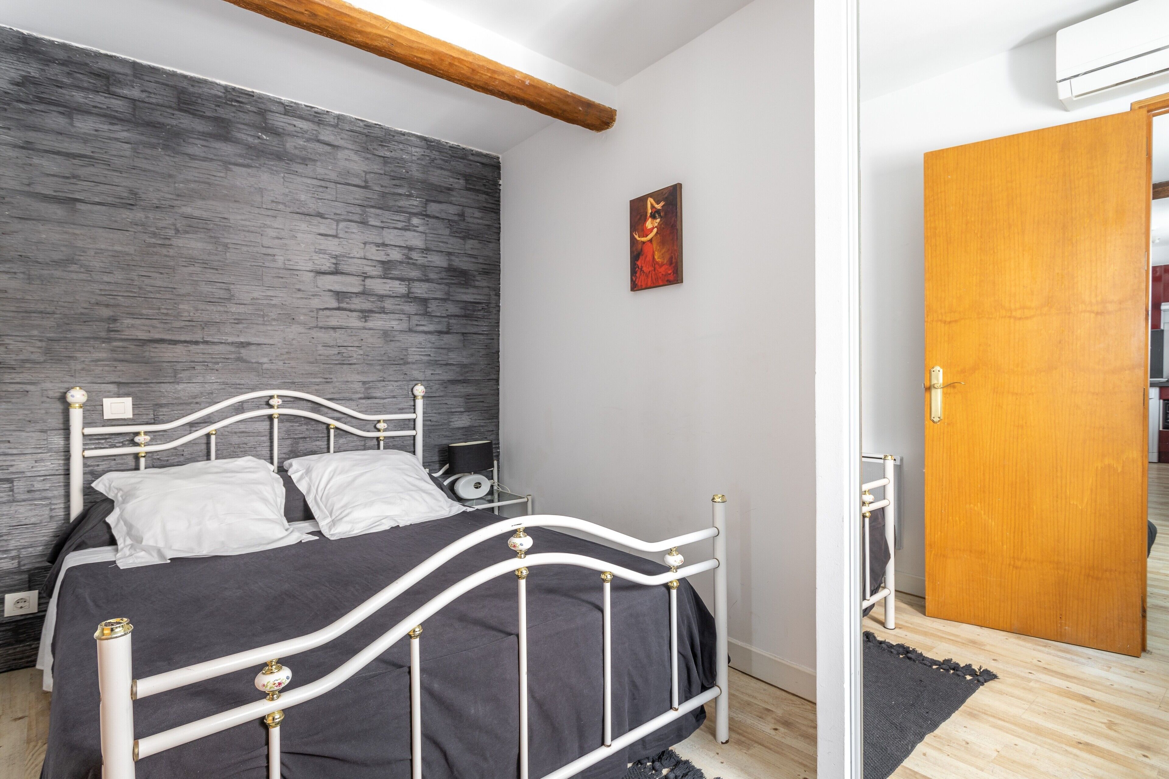 A bedroom with a bed, a wooden door, a wall with a textured surface, and a painting.