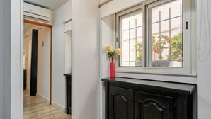 Un couloir doté d’un plancher en bois, d’une armoire noire, d’une fenêtre donnant sur la verdure et d’un vase rouge contenant des fleurs.