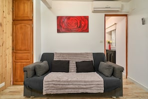 A room with a grey sofa, a red rose painting on the wall, and a wooden door.