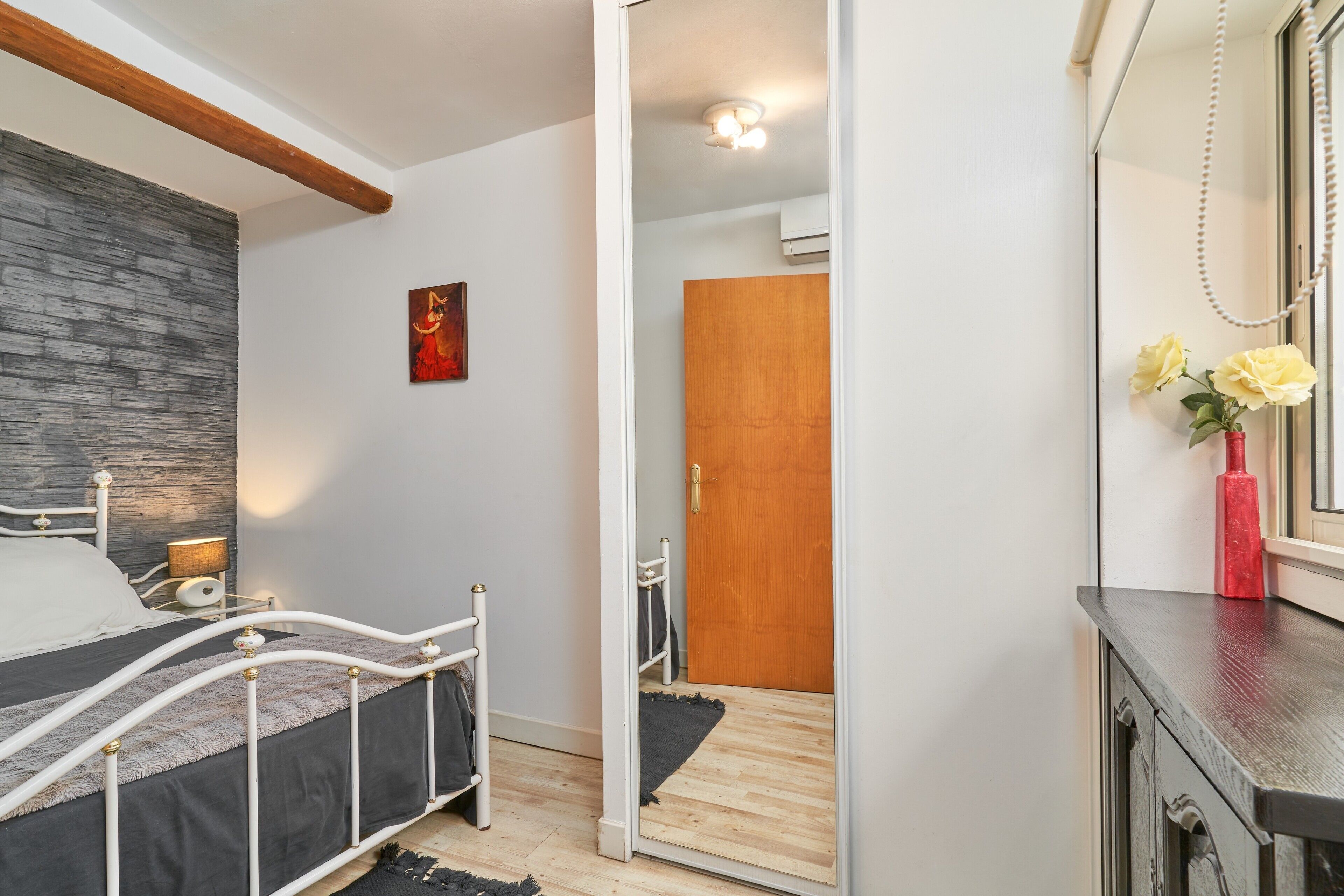 Une chambre à coucher comprenant un lit, un miroir, une commode et une porte donnant sur une autre pièce.