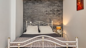 Un lit avec un cadre en métal blanc, deux oreillers, une couverture moelleuse et un mur orné d’un motif texturé.