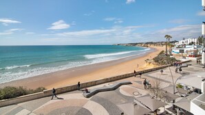 Un paseo marítimo costero con una playa, un sendero curvo y edificios al fondo.