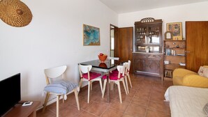 Una habitación con una mesa de comedor, sillas, un televisor, una estantería y una cama.