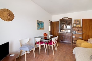A room with a dining table, chairs, a TV, a bookshelf, and a bed.