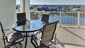 Un balcon doté d’une table en verre et de quatre chaises, offrant une vue sur un quartier résidentiel avec des maisons et une étendue d’eau.