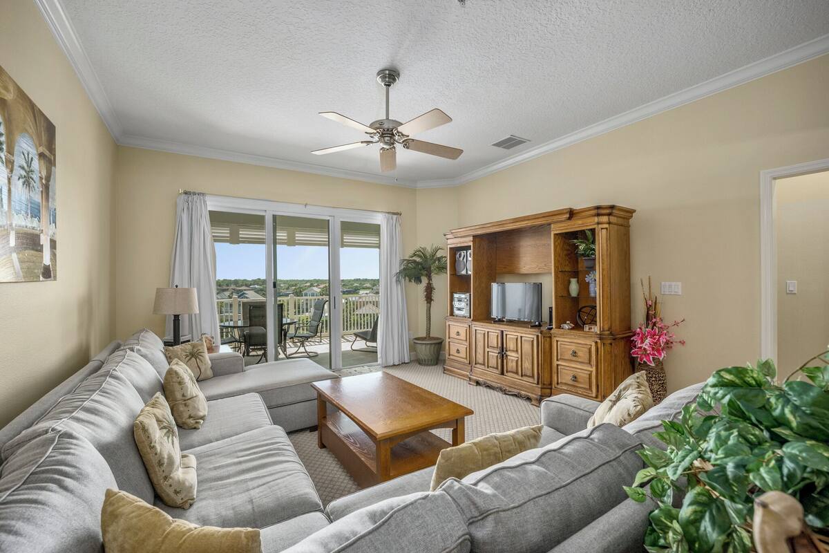 A living room with a grey sofa, a wooden coffee table, a television on a wooden cabinet, and a ceiling fan.