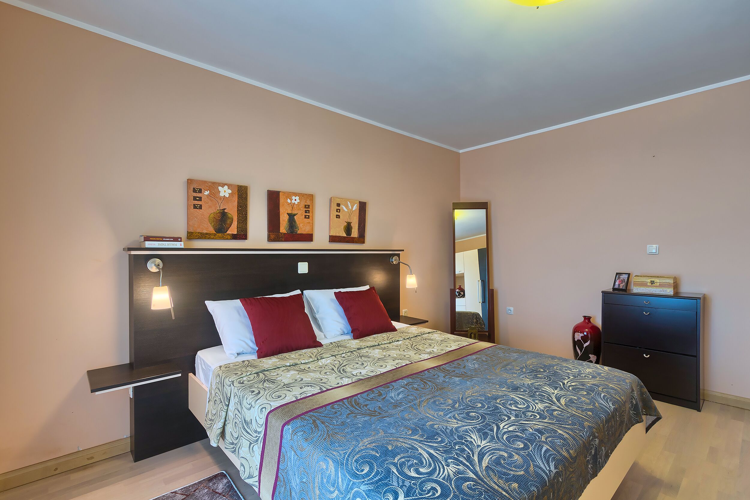 A bedroom with a bed, bedside tables, a dresser, and wall art.