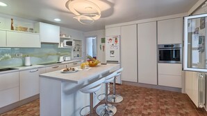 Une cuisine moderne avec des meubles blancs, un îlot central doté de tabourets, un four à micro-ondes et un réfrigérateur.