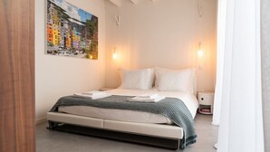 A bedroom with a bed, bedside tables, a painting on the wall, and a window with curtains.