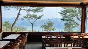 A restaurant with wooden tables and chairs, large windows offering a view of trees and mountains.