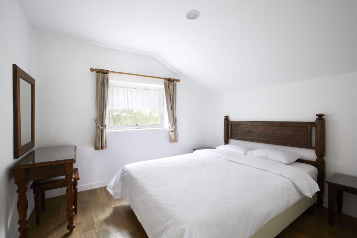 Quarto com cama de madeira, mesa de cabeceira, cortinas na janela e luminária no teto.