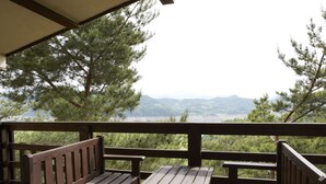 A wooden deck with benches and a table, overlooking a forested area and distant mountains.