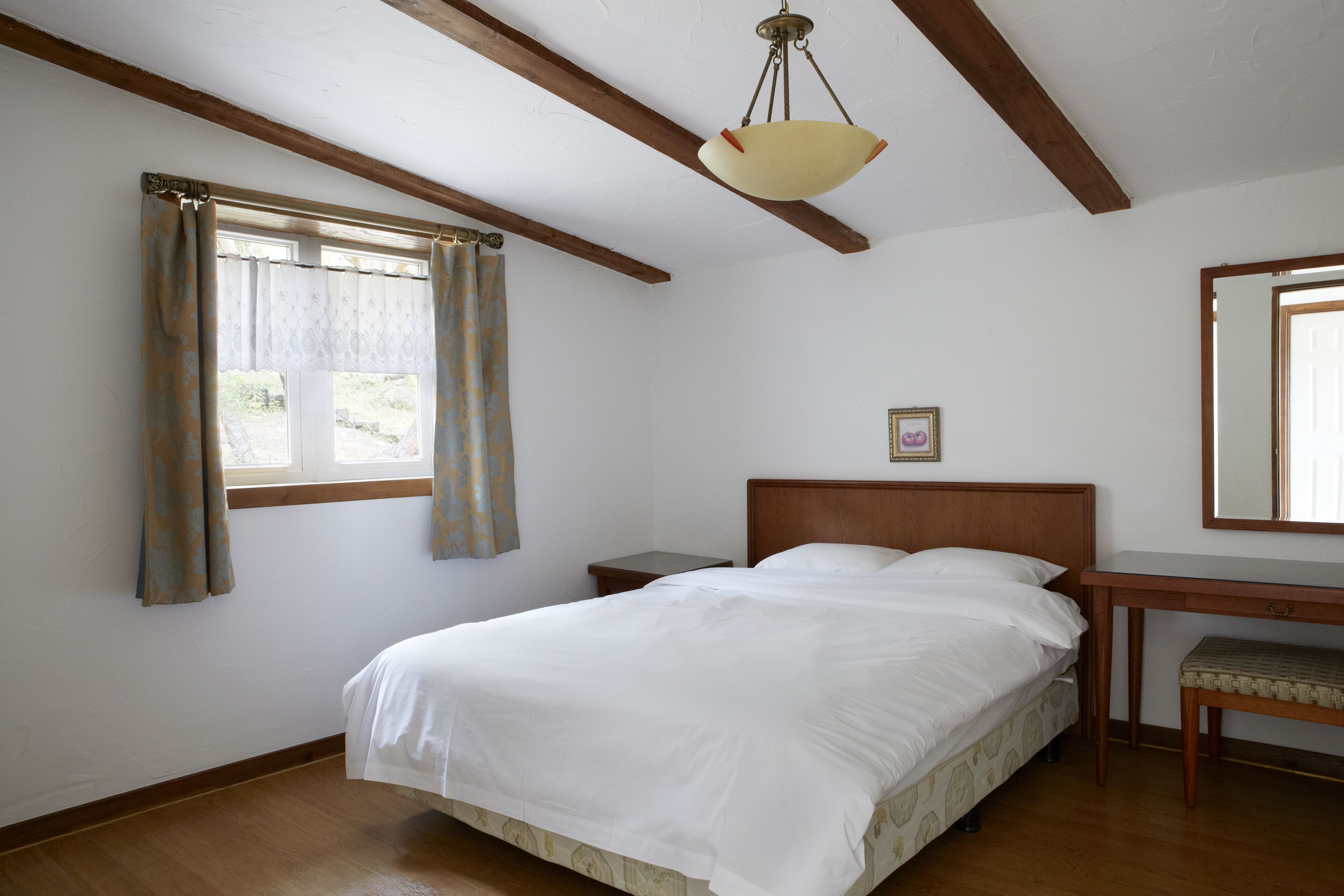 A bedroom with a bed, wooden headboard, bedside table, and a hanging light fixture.