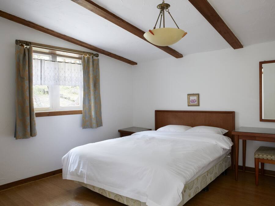 A bedroom with a bed, wooden headboard, bedside table, and a hanging light fixture.
