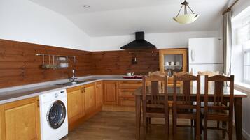 A kitchen with wooden cabinets, a built-in washing machine, a dining table with chairs, and a hanging light fixture.