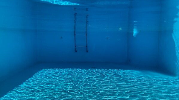 An underwater view of a swimming pool with a ladder.