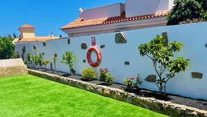 A well-maintained garden with a white wall, a red lifebuoy, and a stone border. - Luxury Villa on Golf Resort (fuerteventura)