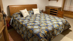 A bedroom with a wooden bed, two decorative pillows, a nightstand, a dresser, and a wooden cabinet.