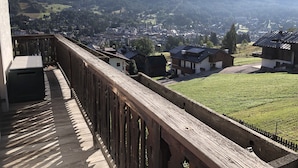 A wooden balcony overlooking a town with houses and mountains in the background.