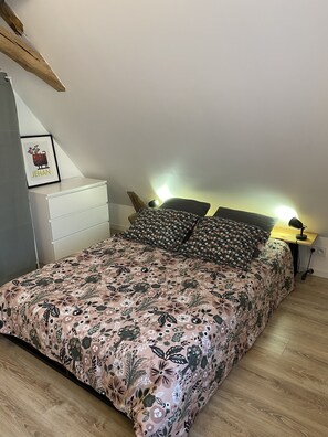 A bedroom with a floral bedspread, a white dresser, a framed picture on the wall, and a bedside lamp.