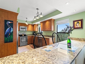 A kitchen with granite countertops, wooden cabinets, stainless steel appliances, and a dining area with chairs and a table. - Reflections on the Gulf by Distinctive Beach Rentals (Indian Rocks Beach)
