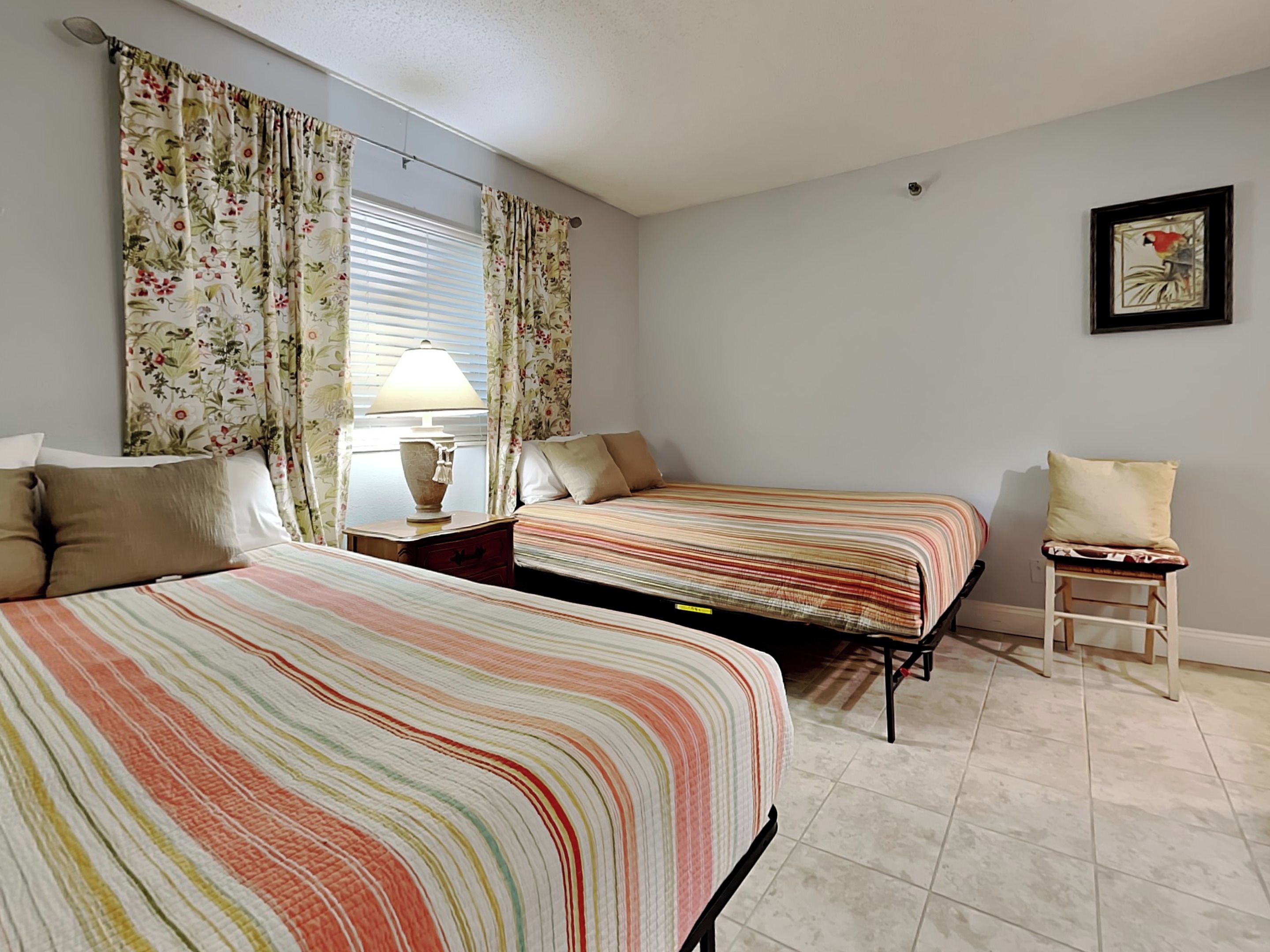 Un dormitorio con dos camas, una mesita de noche, una silla y una lámpara.