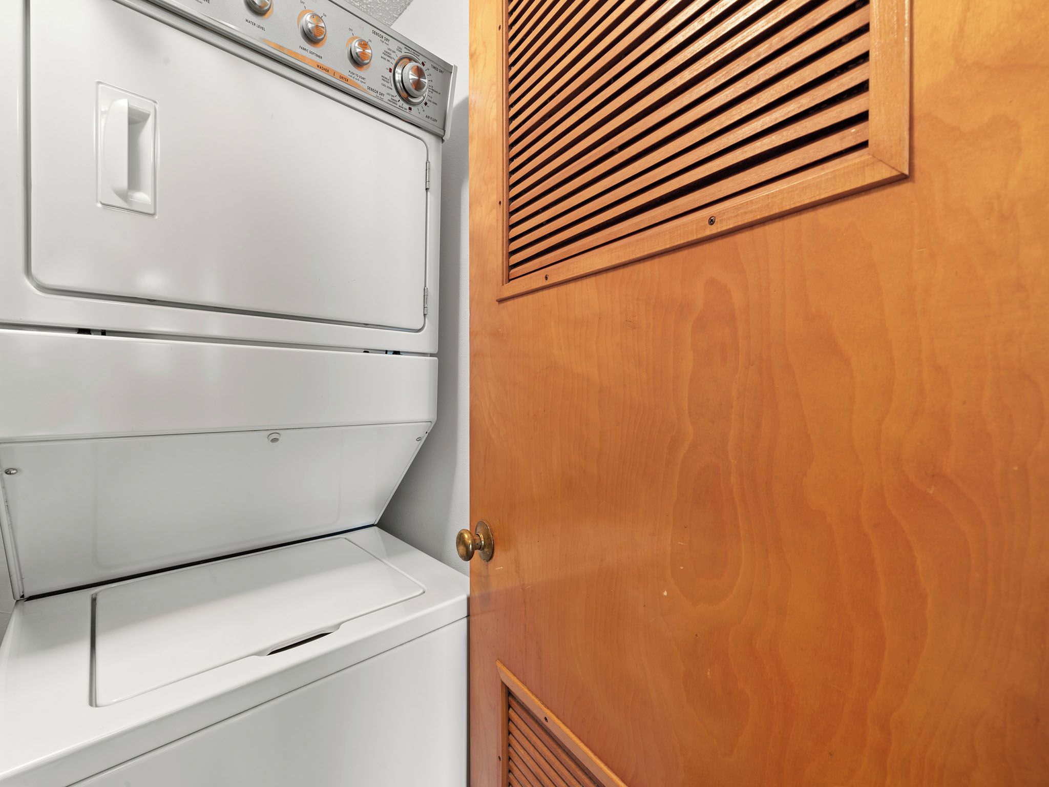 Un sèche-linge blanc et une porte en bois dotée d’une grille d’aération.