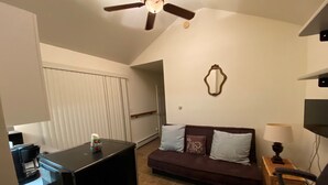Un salon avec un canapé de couleur foncée, un téléviseur, un ventilateur de plafond et un miroir fixé au mur.