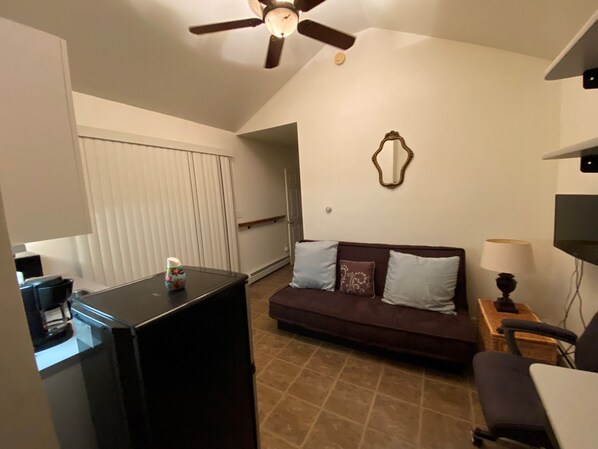 A living room with a dark-colored sofa, a television, a ceiling fan, and a wall-mounted mirror. - One Bedroom Unit in Malta/Saratoga (Malta)