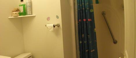 A bathroom with a toilet, a shower with a grab bar, a sink, and a toilet paper holder.