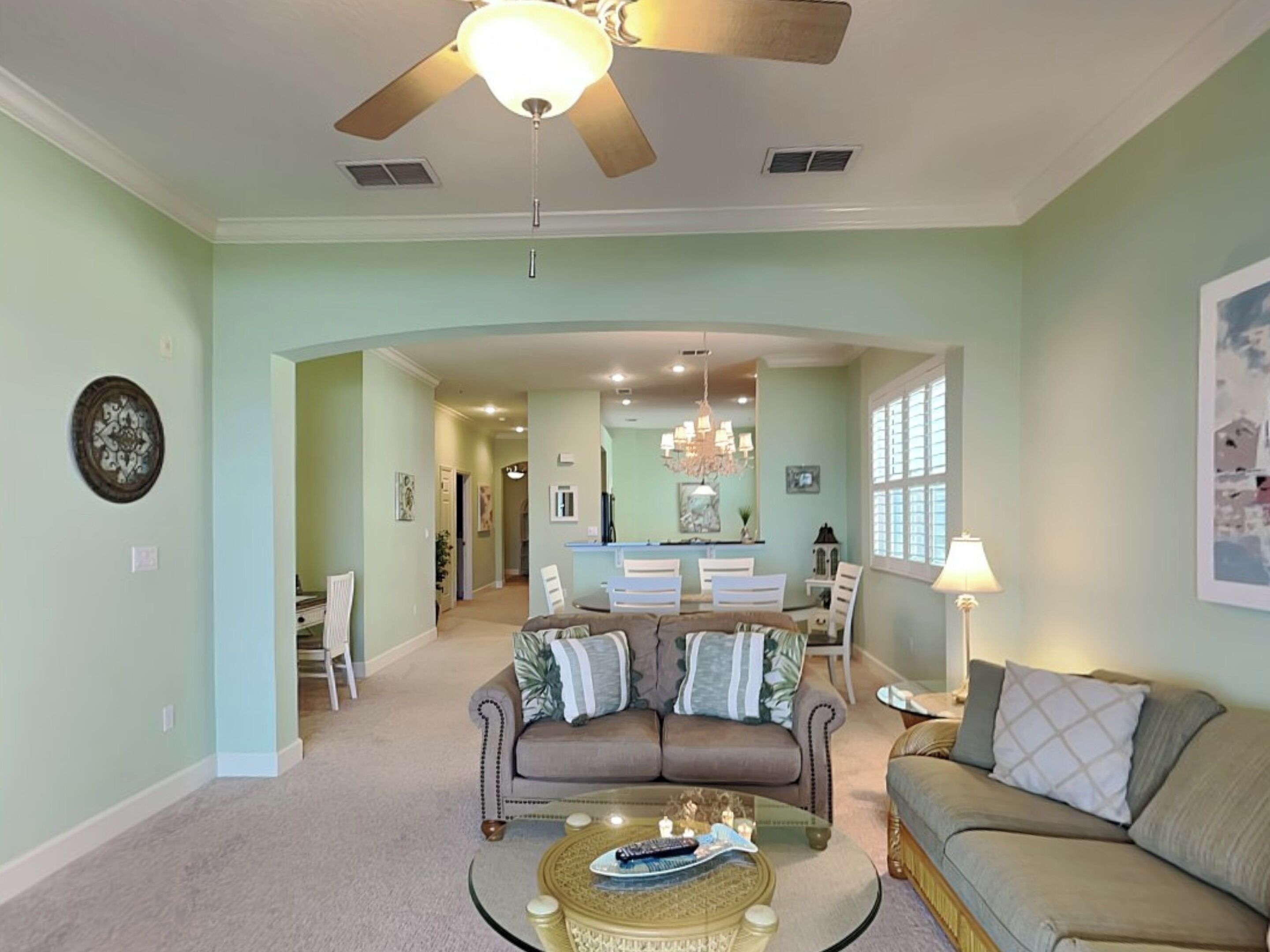 A living room with a ceiling fan, a dining area with a chandelier, and a kitchen in the background.