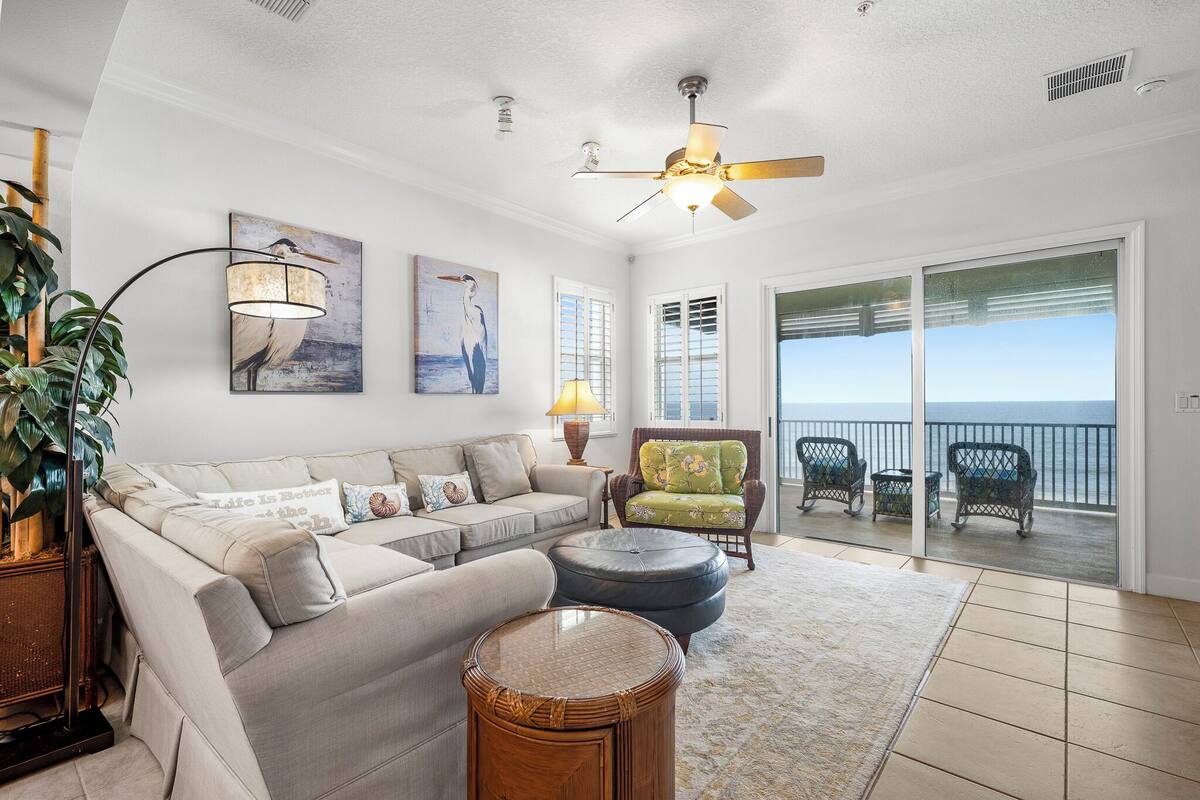A living room with a sofa, armchairs, a round table, and a balcony with a view.