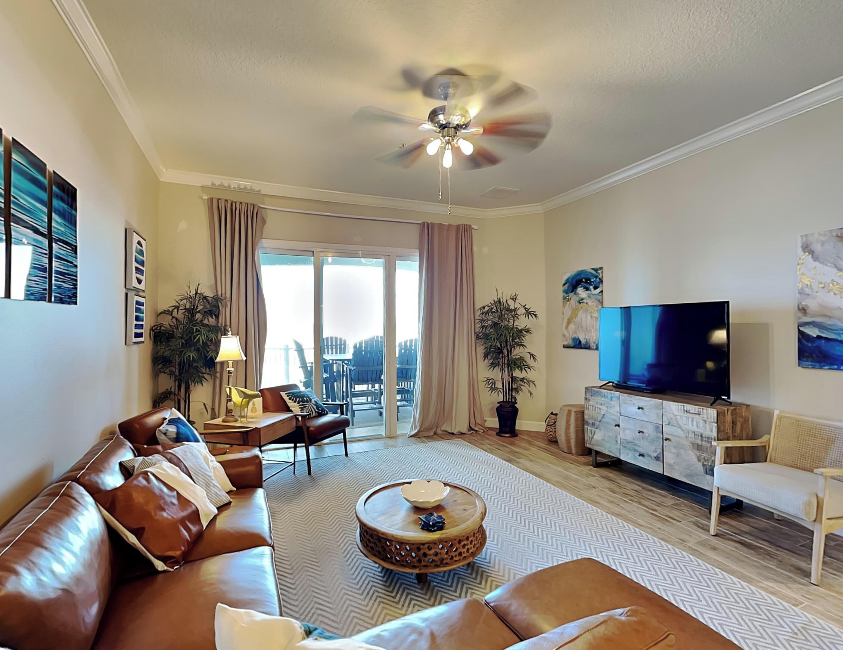 A modern living room with a brown leather sofa, a round coffee table, a TV, and a ceiling fan.