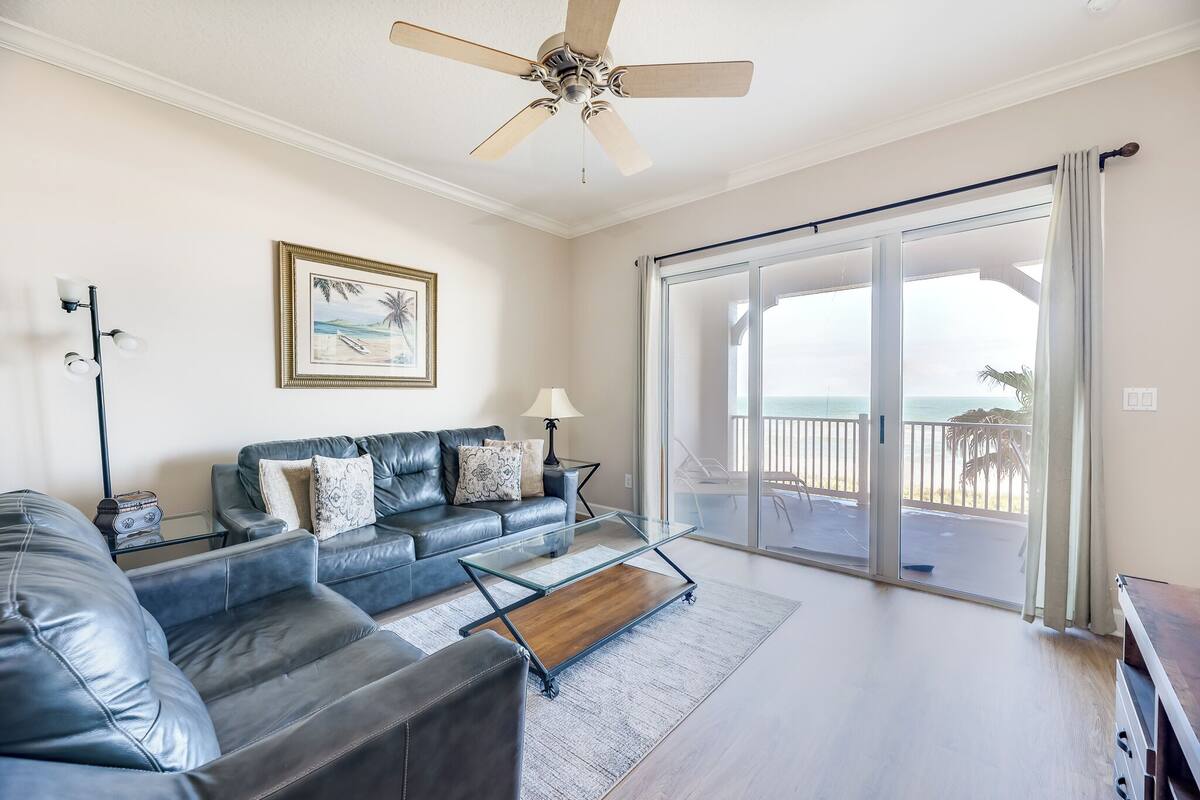 A living room with a sofa, coffee table, and a view of the ocean through a sliding glass door.
