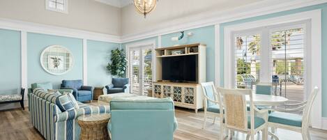 A spacious living room with a sectional sofa, a television, and a dining area with white chairs and a table.