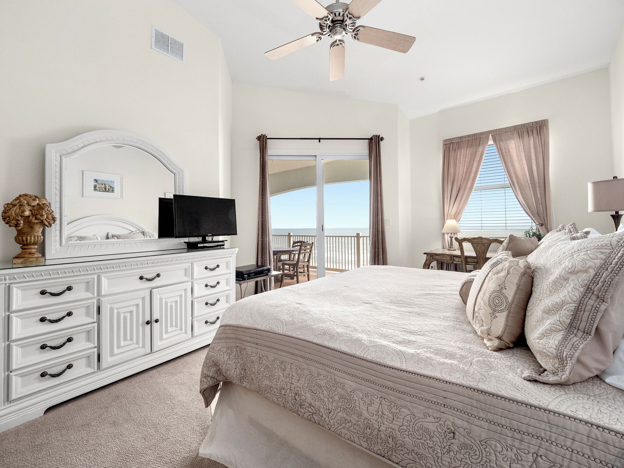 A bedroom with a bed, a dresser, a television, and a balcony with a view.
