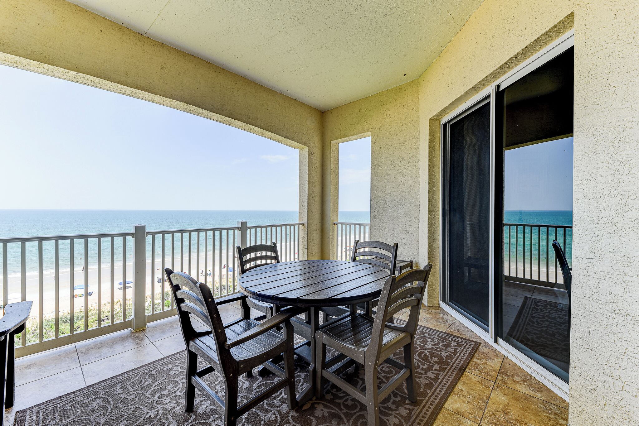 A covered patio with a table and chairs, a view of the beach, and a sliding glass door.