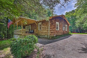 A wooden cabin with a porch and a flag, surrounded by trees. - Near Hiking: Roaring Gap Retreat w/ Fire Pit! (Roaring Gap)