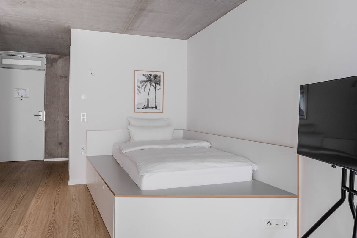 Un dormitorio minimalista con cama, televisión y un cuadro en la pared.