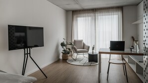 A modern living room with a flat-screen TV on a tripod stand, a round wooden table, a laptop, a chair, and a potted plant. - CLOUD No7 STUDIOS (Tuebingen)