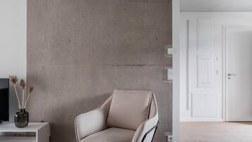 A modern living room with a beige armchair, a white console table with a vase, and a concrete accent wall.
