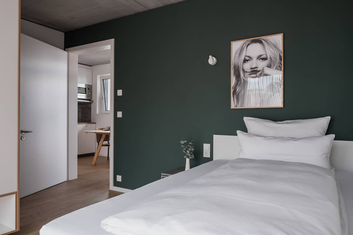 Un dormitorio moderno con una cama grande, una pared verde oscuro y un cuadro enmarcado.