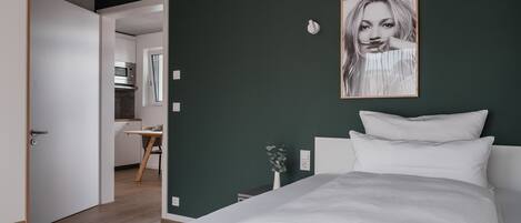 A modern bedroom with a large bed, a dark green wall, and a framed picture.
