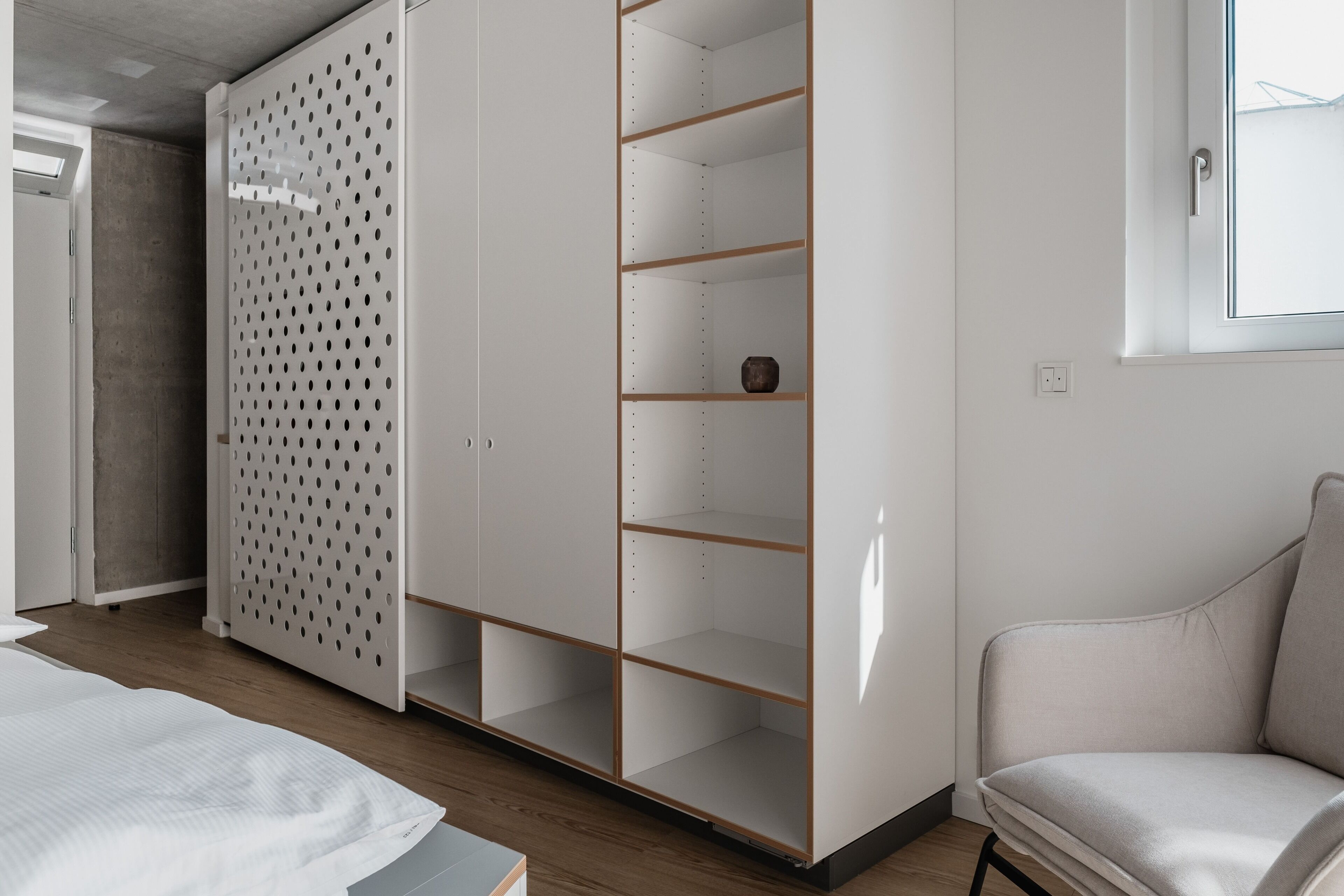 A bedroom with a bed, a wardrobe, a chair, and a window.