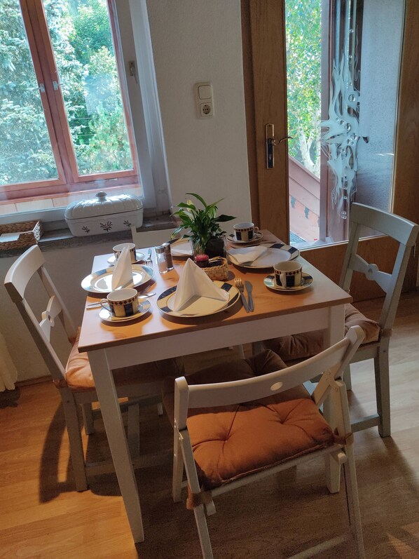 A dining table set with plates, cups, and cutlery, surrounded by chairs with cushions.